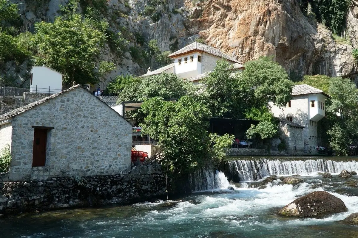 Kamena kuća uz rijeku i slap podno stjenovite litice u Hercegovini